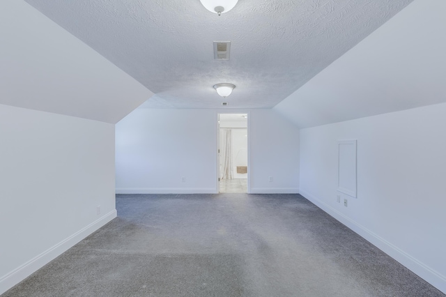 additional living space with carpet, baseboards, visible vents, lofted ceiling, and a textured ceiling