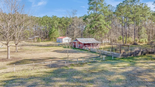 view of yard featuring an outbuilding, fence, a wooded view, a rural view, and dirt driveway