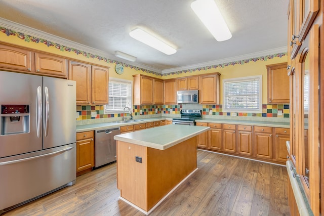 kitchen with a sink, hardwood / wood-style floors, stainless steel appliances, light countertops, and a healthy amount of sunlight