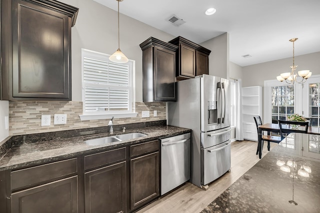 kitchen featuring dark brown cabinets, light wood-type flooring, dark stone countertops, appliances with stainless steel finishes, and a sink