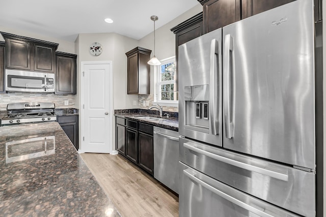 kitchen with a sink, appliances with stainless steel finishes, dark stone countertops, and dark brown cabinets