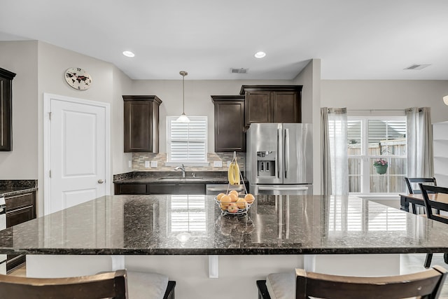 kitchen with visible vents, dark brown cabinets, a kitchen bar, stainless steel fridge, and a sink