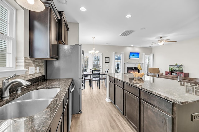 kitchen with dark brown cabinets, visible vents, a lit fireplace, and a sink