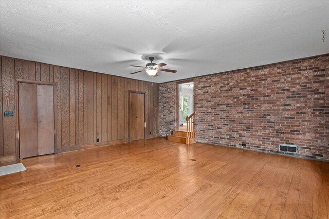 1019 Pinon Rd, North Augusta, SC 29841 - unfurnished living room featuring ceiling fan, light wood-style flooring, brick wall, a textured ceiling, and wood walls