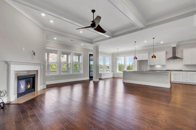 unfurnished living room with beam ceiling, sink, crown molding, a fireplace, and ceiling fan with notable chandelier