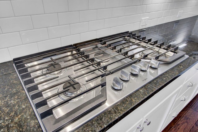 details with white cabinets, backsplash, stainless steel gas cooktop, and dark stone counters