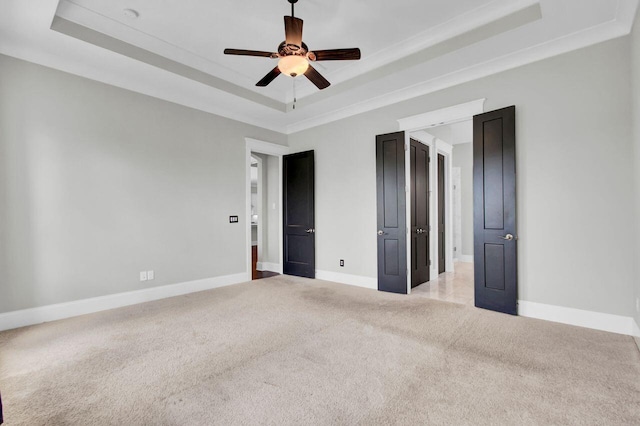 unfurnished bedroom featuring a tray ceiling, ceiling fan, light colored carpet, and ornamental molding