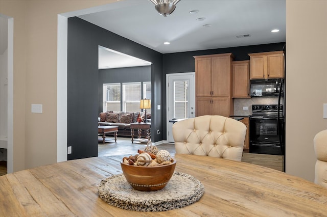 kitchen featuring tasteful backsplash, wood-type flooring, butcher block counters, and black appliances