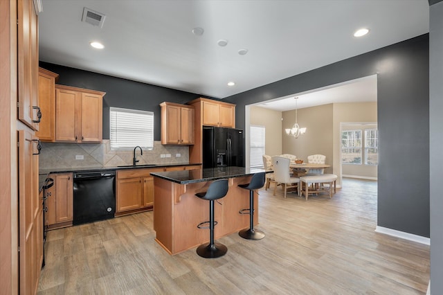 kitchen featuring sink, dark stone countertops, a kitchen bar, a center island, and black appliances