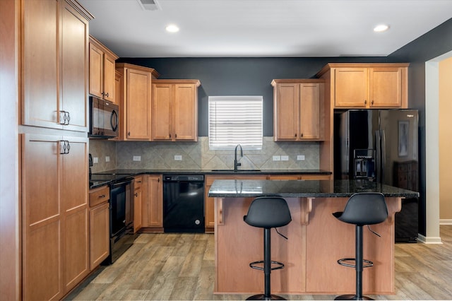 kitchen with sink, a center island, a kitchen breakfast bar, dark stone counters, and black appliances