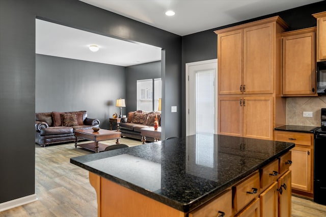 kitchen featuring decorative backsplash, light hardwood / wood-style flooring, dark stone counters, and a kitchen island