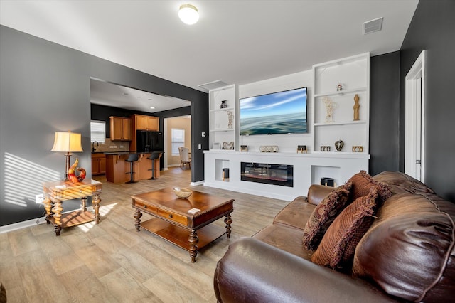 living room featuring sink, built in features, and light wood-type flooring