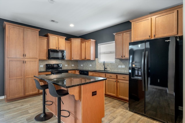 kitchen with sink, a center island, dark stone counters, light hardwood / wood-style floors, and black appliances