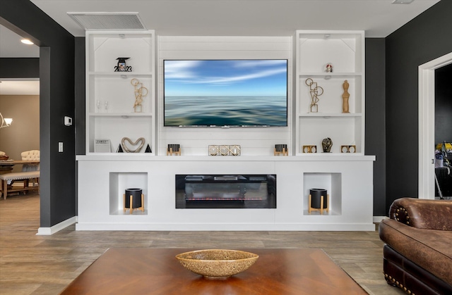 living room with hardwood / wood-style flooring, built in features, and a large fireplace