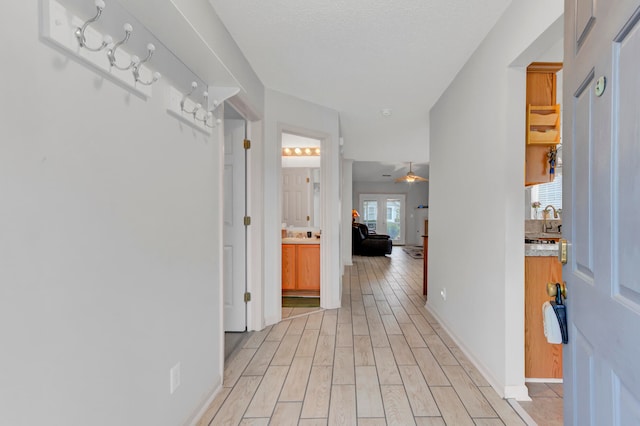 hallway with a textured ceiling, sink, and light wood-type flooring