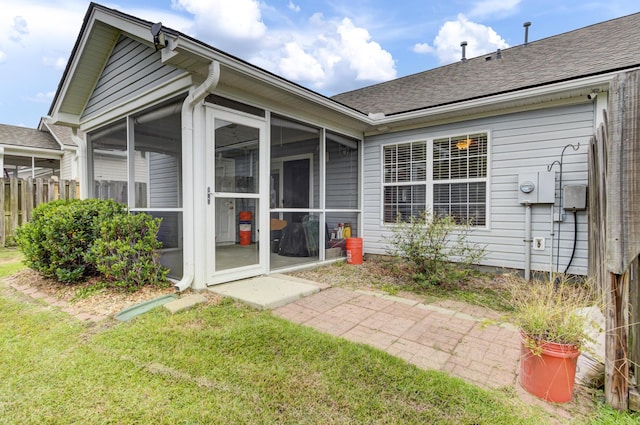 rear view of property featuring a yard, a sunroom, a shingled roof, and fence