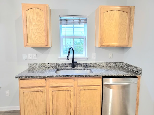 kitchen with light brown cabinetry, stainless steel dishwasher, dark stone countertops, and sink