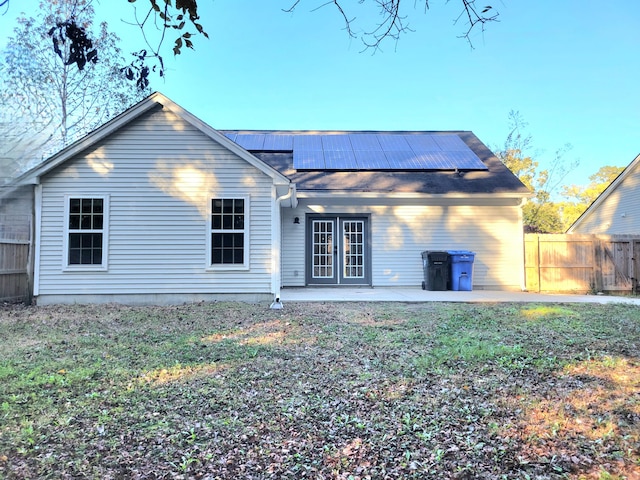 rear view of house with a lawn, french doors, a patio, and solar panels