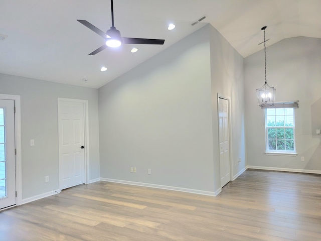 spare room with ceiling fan with notable chandelier, light hardwood / wood-style floors, and lofted ceiling