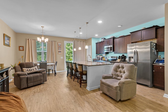 kitchen featuring appliances with stainless steel finishes, hanging light fixtures, a breakfast bar area, a center island with sink, and light hardwood / wood-style floors