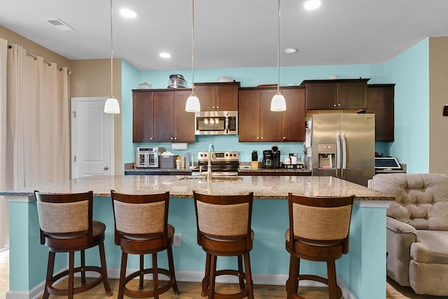 kitchen with appliances with stainless steel finishes, a center island with sink, a kitchen bar, and decorative light fixtures