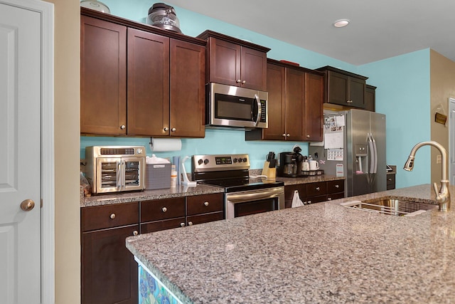 kitchen featuring stainless steel appliances, dark brown cabinetry, sink, and light stone counters