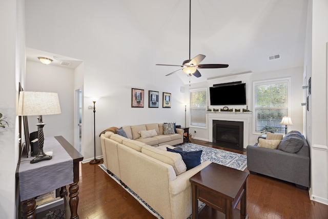 living room featuring ceiling fan, a towering ceiling, and dark wood-type flooring