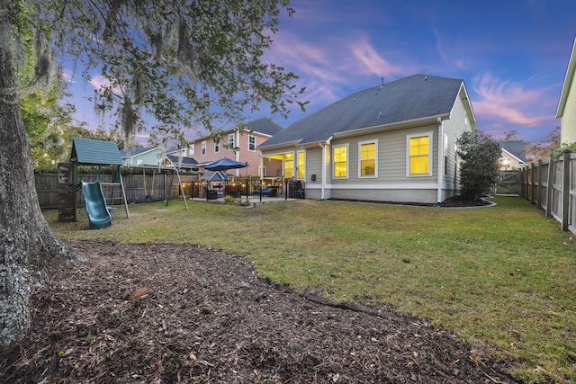 back house at dusk featuring a yard and a playground