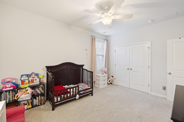 bedroom with a crib, light colored carpet, and ceiling fan