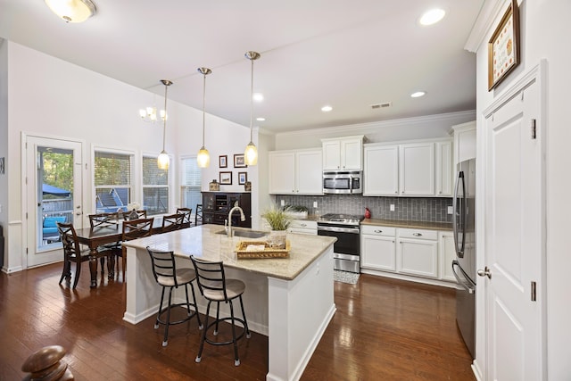 kitchen with light stone countertops, appliances with stainless steel finishes, white cabinets, dark hardwood / wood-style floors, and hanging light fixtures