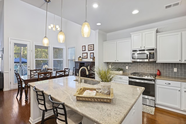 kitchen with white cabinets, appliances with stainless steel finishes, a center island with sink, and sink