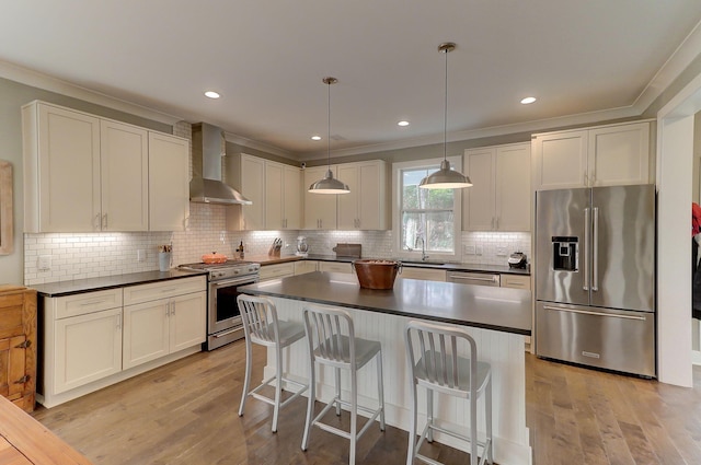 kitchen featuring pendant lighting, light hardwood / wood-style floors, wall chimney range hood, appliances with stainless steel finishes, and backsplash