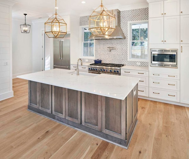 kitchen featuring high end appliances, backsplash, light hardwood / wood-style flooring, wall chimney exhaust hood, and white cabinets