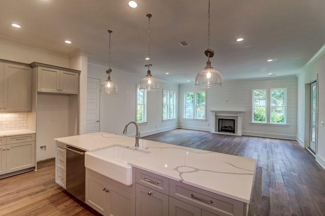 kitchen featuring pendant lighting, light stone counters, crown molding, dishwasher, and hardwood / wood-style flooring