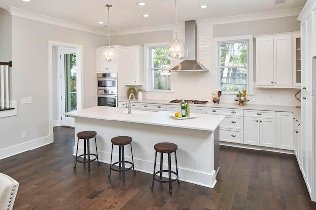 kitchen featuring white cabinetry, a center island with sink, wall chimney exhaust hood, dark hardwood / wood-style flooring, and ornamental molding