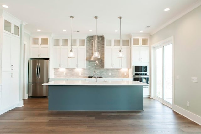 kitchen with wall chimney exhaust hood, hanging light fixtures, stainless steel appliances, and a kitchen island with sink