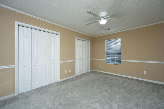 unfurnished bedroom featuring light carpet, ornamental molding, a textured ceiling, ceiling fan, and multiple closets