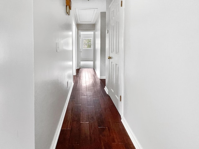 hall featuring baseboards, attic access, and dark wood-style flooring