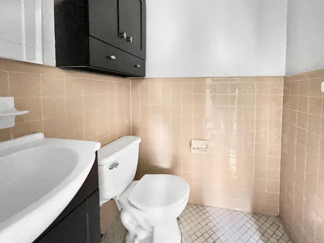 half bath featuring tile patterned flooring, toilet, tile walls, and vanity