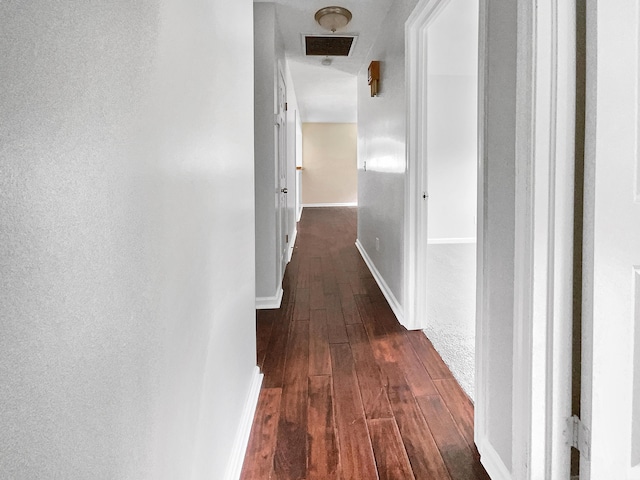 hallway featuring visible vents, baseboards, and dark wood-style flooring