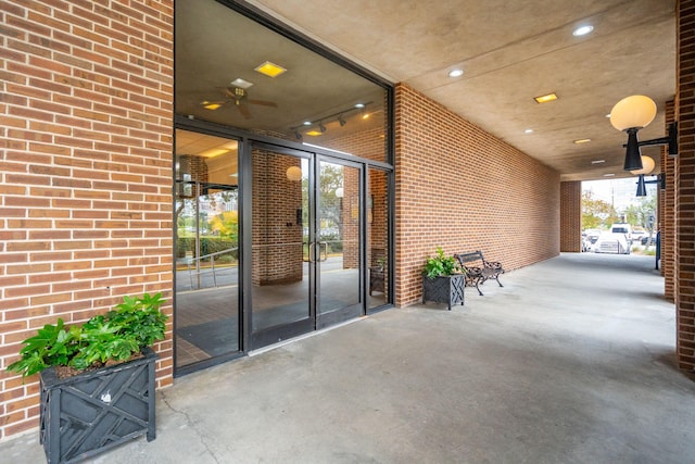 entrance to property featuring a ceiling fan, a patio area, and brick siding