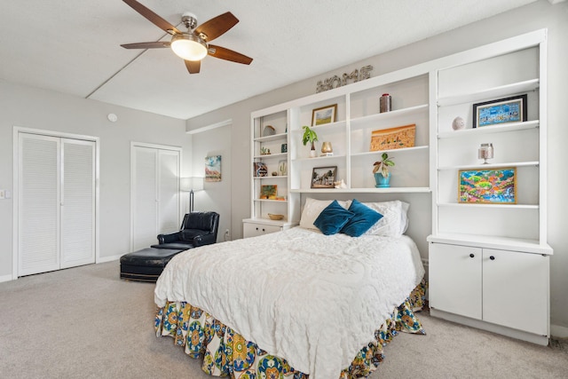 bedroom with light carpet, a textured ceiling, a ceiling fan, and multiple closets