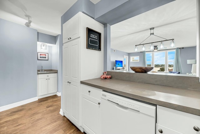 kitchen with light wood-type flooring, white dishwasher, sink, pendant lighting, and white cabinets