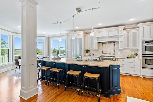 kitchen with a sink, appliances with stainless steel finishes, a kitchen island with sink, white cabinets, and backsplash
