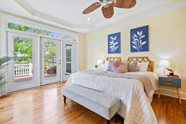 bedroom featuring access to exterior, a tray ceiling, ornamental molding, wood finished floors, and baseboards