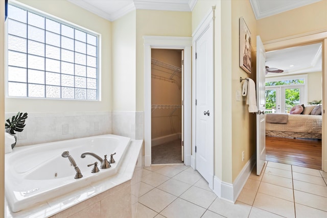 ensuite bathroom featuring tile patterned floors, ornamental molding, a tub with jets, baseboards, and a walk in closet
