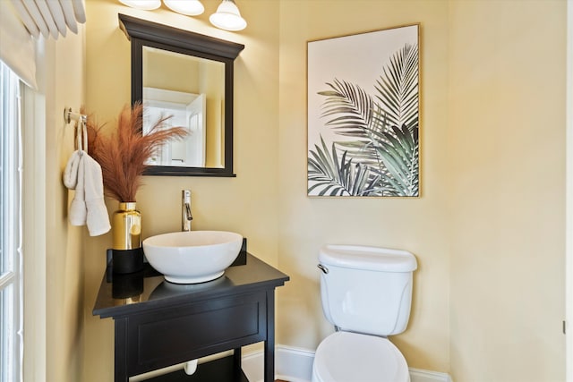 half bath with baseboards, toilet, and vanity