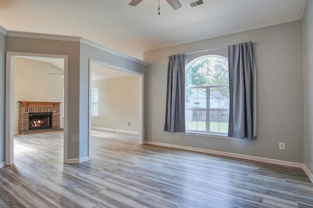 spare room featuring a textured ceiling, light hardwood / wood-style flooring, ceiling fan, and a brick fireplace