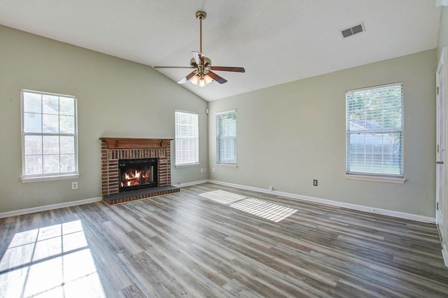 unfurnished living room featuring vaulted ceiling, a wealth of natural light, a brick fireplace, and ceiling fan