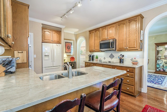 kitchen with light stone counters, arched walkways, a sink, white refrigerator with ice dispenser, and stainless steel microwave